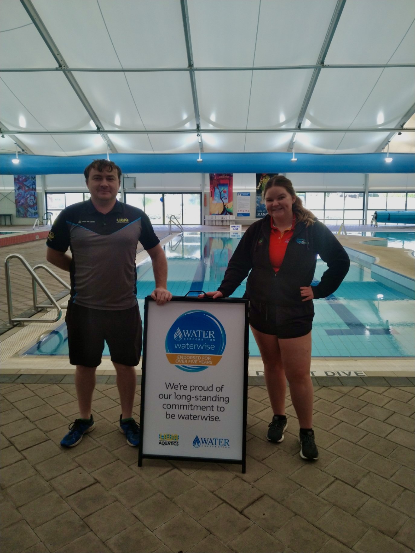Two AquaCentre staff members with the Waterwise five years A-frame sign.