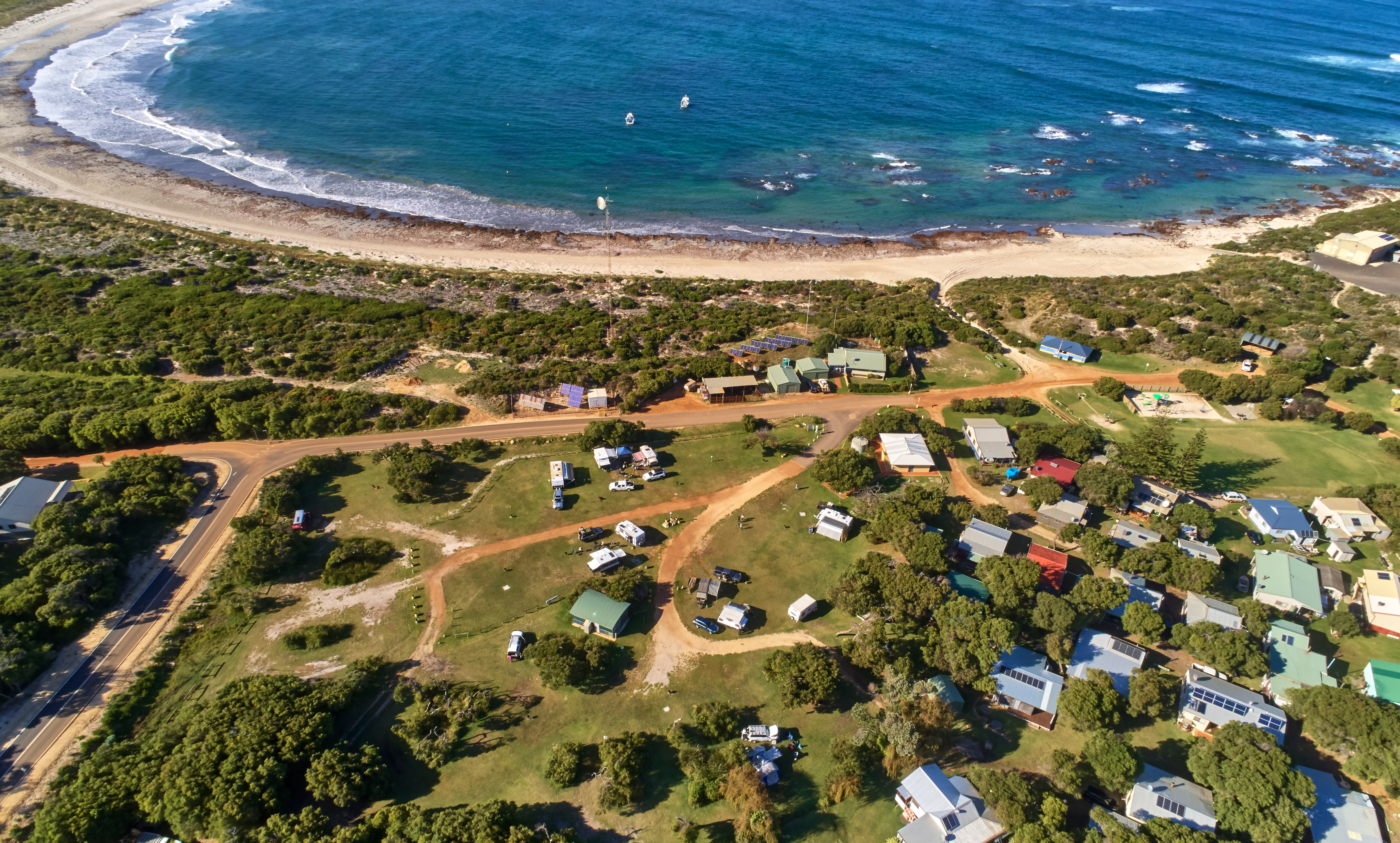 Drone picture of caravans in campground with beach and ocean in the backdrop.