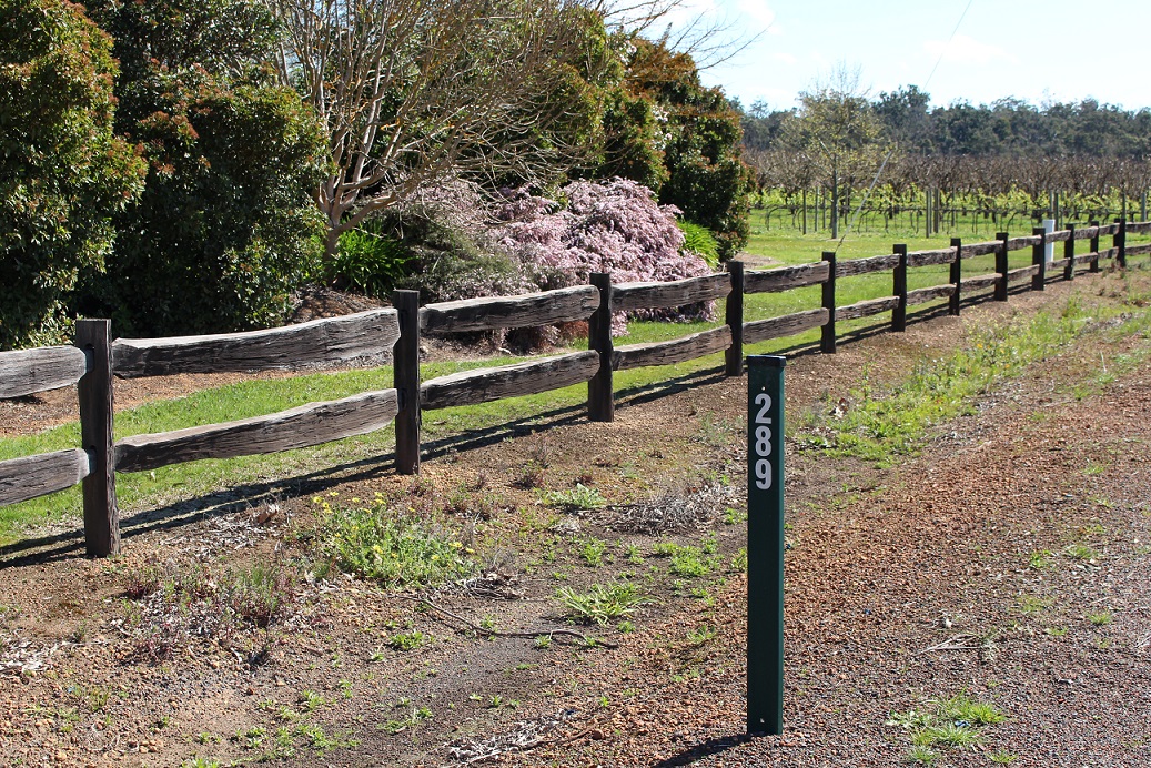 green post rural road numbering outside of property with trees and fenceline