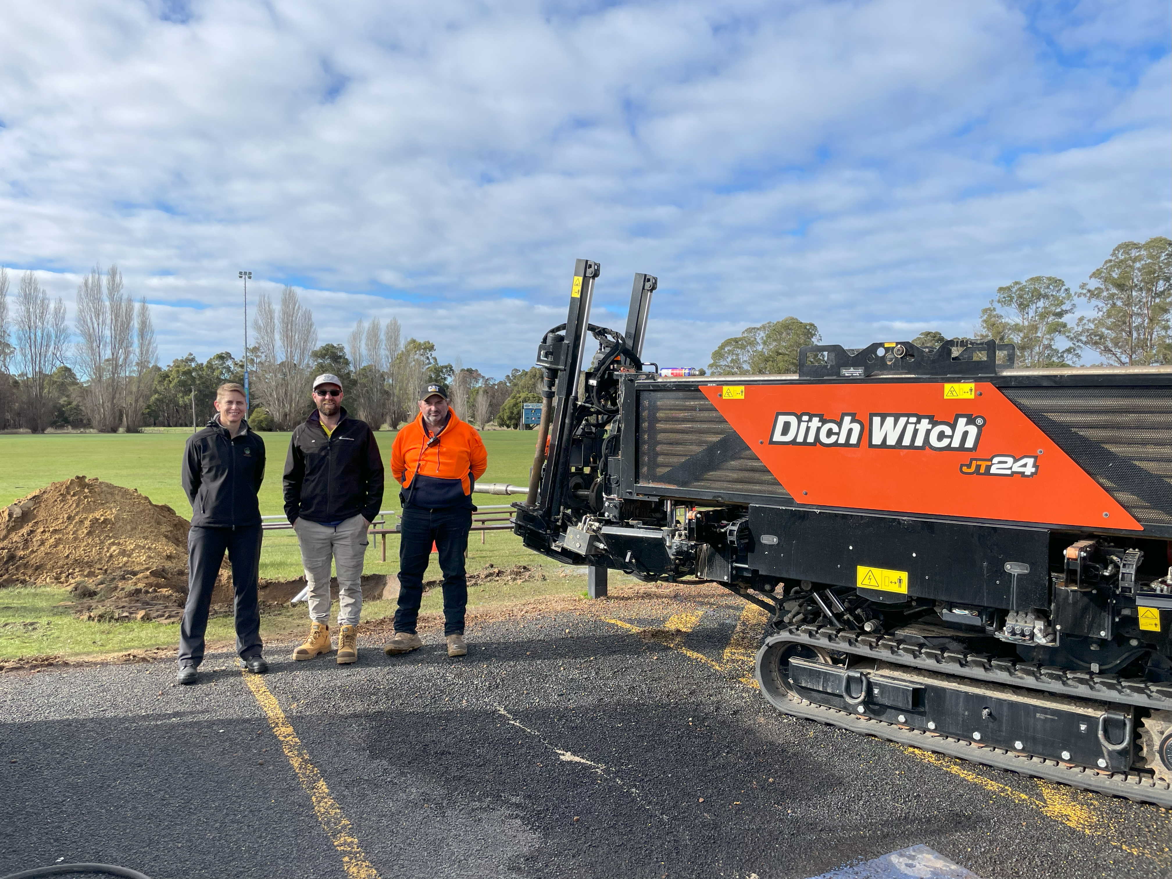 Three people standing next to a ditch witch machine.